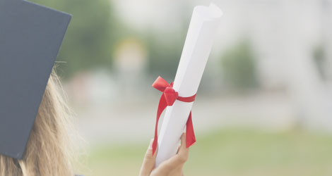 Bildausschnitt zeigt Studentin mit Doktorhut von hinten, sie hält ihr eingerolltes Abschlusszeugnis in der Hand