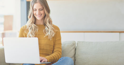 Studentin sitzt auf Sofa mit Laptop auf dem Schoß