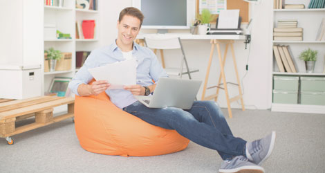 Student sitzt auf Sitzsack mit Laptop auf dem Schoß, er hält zwei Papierblätter in den Händen