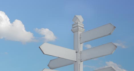 Wegweiser mit weißen Schildern in verschiedene Richtungen vor einem blauen Himmel